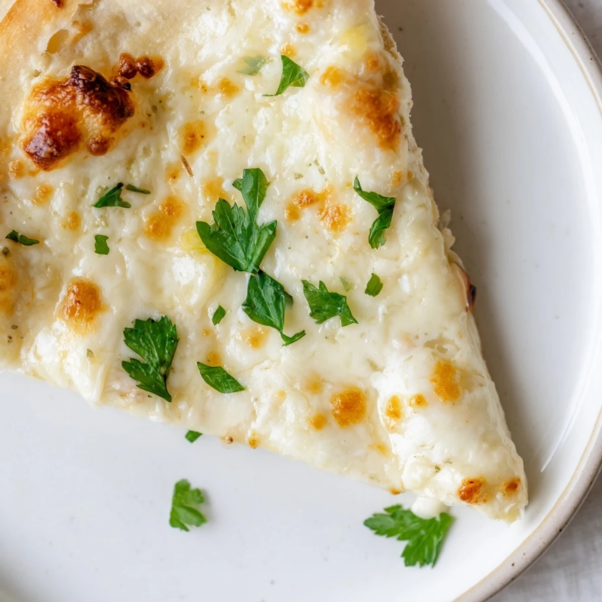 A slice of Creamy Garlic White Pizza showcases the velvety garlic cream sauce and melted cheese.  