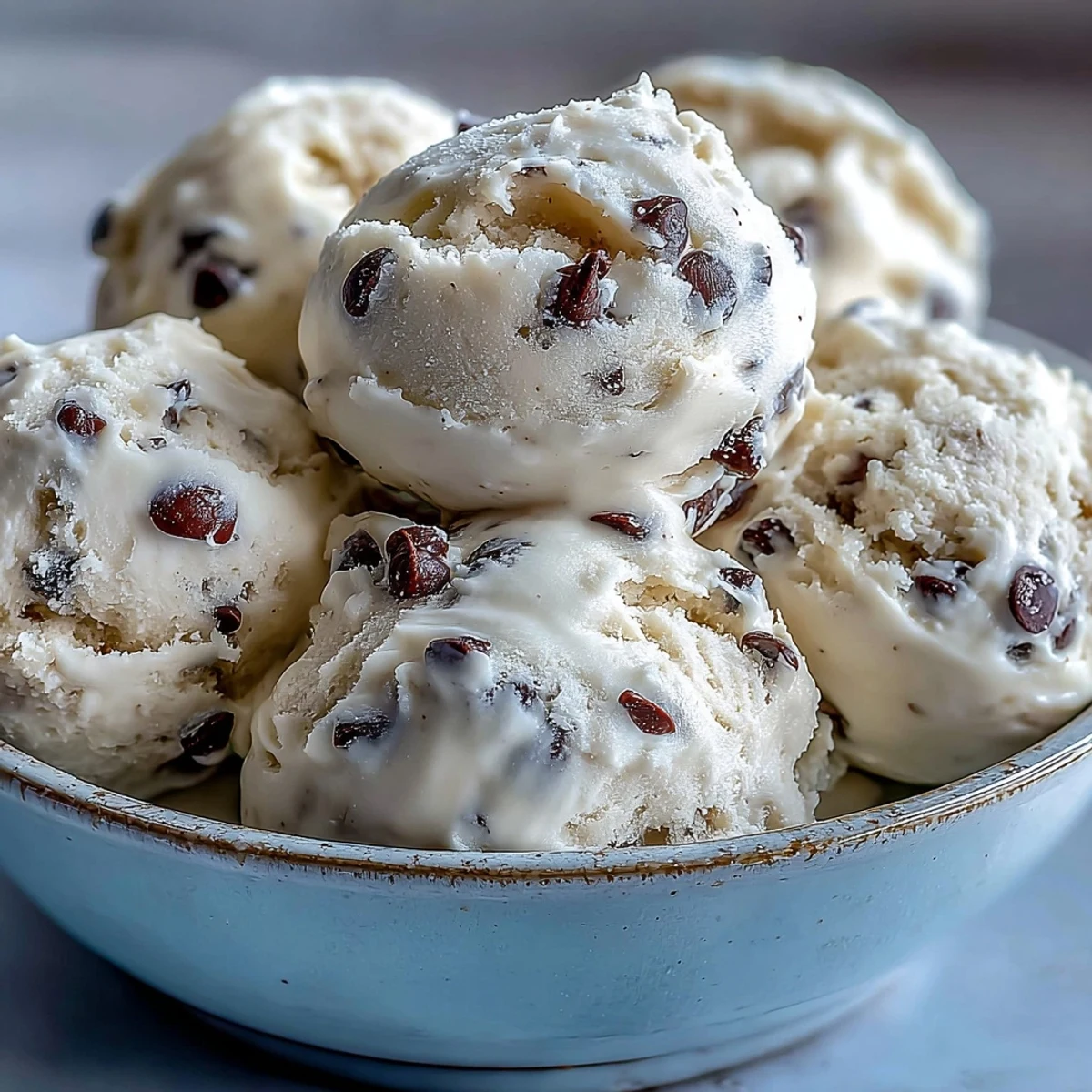 A chilled bowl of Greek Yogurt Cookie Dough, topped with extra chocolate chips, sits beside a glass of milk.