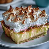 A whole Lemon Meringue Pie sits on a marble counter next to a glass of Moscato.