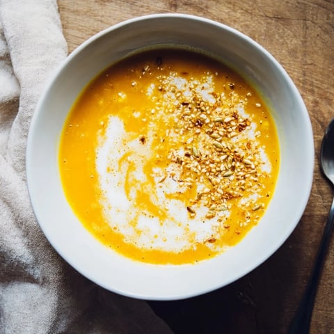 A warm bowl of creamy roasted pumpkin soup boasts toasted seeds on top.