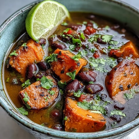 A close-up of creamy Sweet Potato and Black Bean Soup garnished with cilantro, lime, and diced avocado.