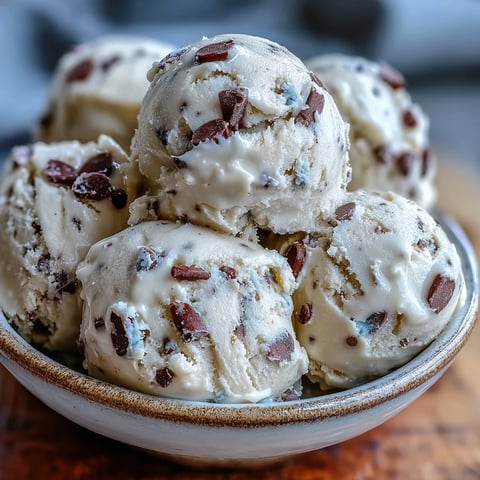 Fresh scoops of Greek Yogurt Cookie Dough showcase creamy texture and abundant mini chocolate chips on a rustic wooden board.