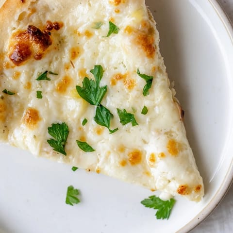 A slice of Creamy Garlic White Pizza showcases the velvety garlic cream sauce and melted cheese.  