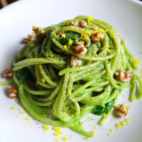 A close-up of Creamy Spinach Walnut Pasta in a white bowl, garnished with lemon zest and freshly ground black pepper.