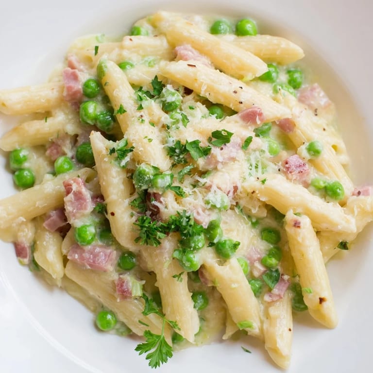 A close-up of Spring Pea & Ham Pasta, featuring bright green peas and golden ham cubes coated in velvety cream sauce.