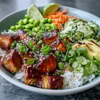 Golden-brown baked salmon cubes glisten atop fluffy white rice in a vibrant Baked Salmon Rice Bowl, garnished with fresh cucumber and carrots.